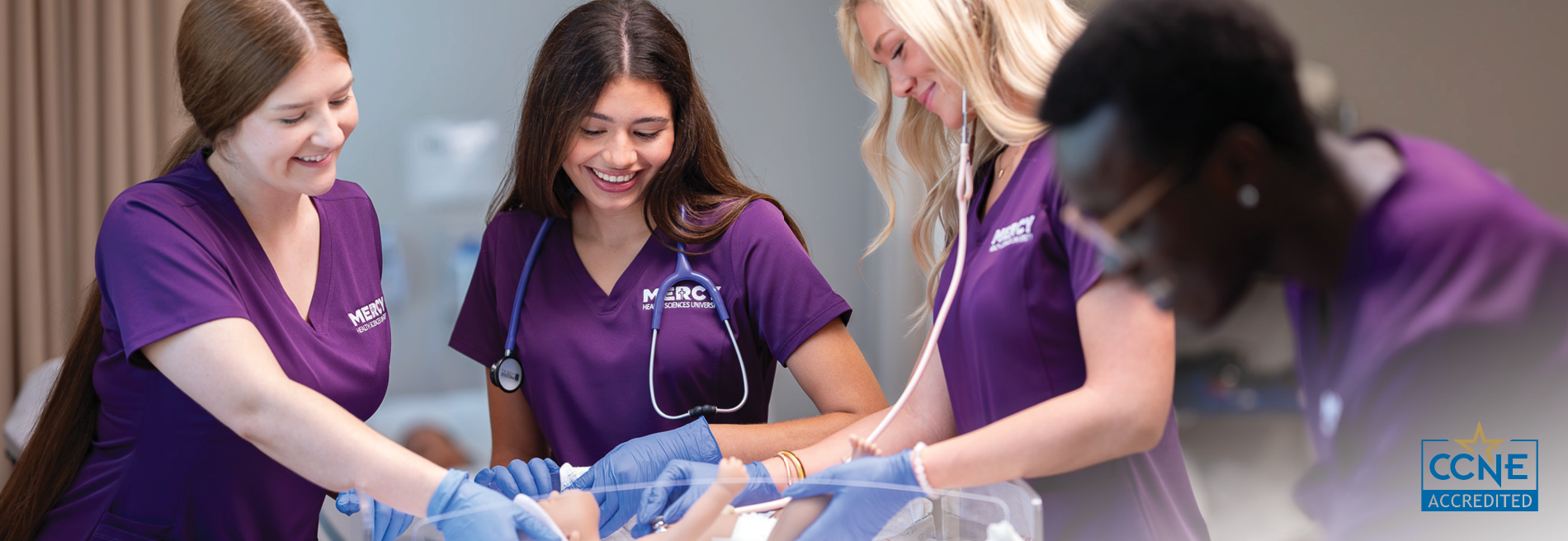 Group of nursing students in Mercy Health Sciences University scrubs practicing infant care procedures with a simulation manikin during hands-on clinical training.