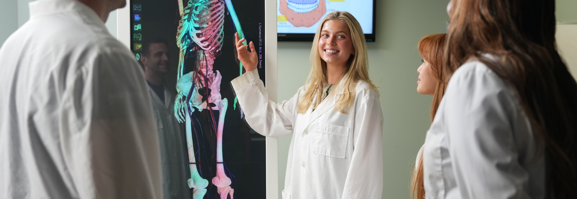 Group of students gathered around an Anatomage Table, examining skeletal and anatomical structures during a hands-on health sciences lesson.