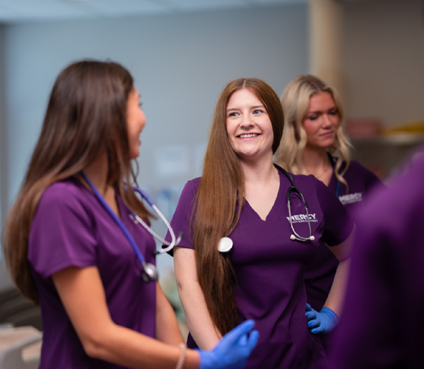 Nursing students in Mercy Health Sciences University scrubs participating in a discussion during hands-on clinical training.