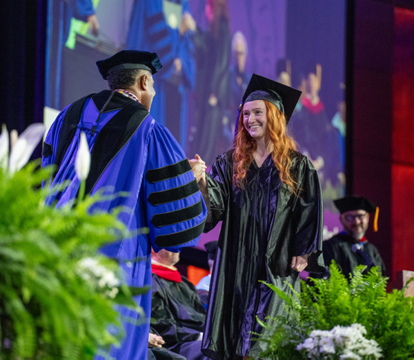 Graduate shaking hands with the college president while crossing the stage during a commencement ceremony.