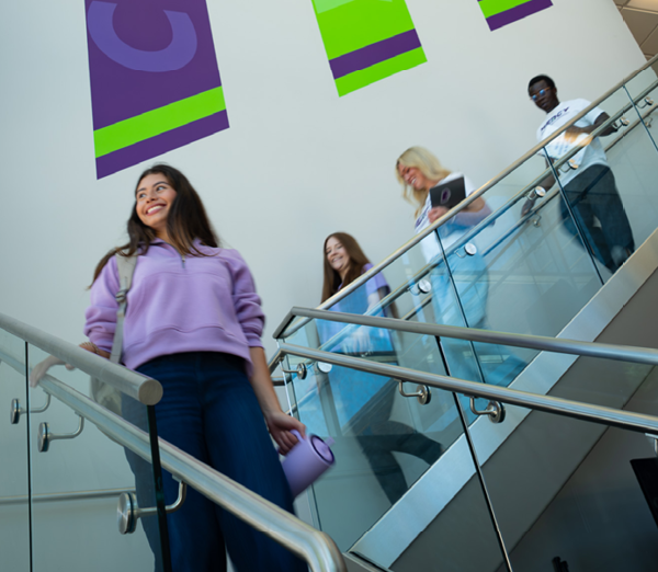 Students walking down a staircase in the ACE lobby, carrying backpacks, laptops, and water bottles.